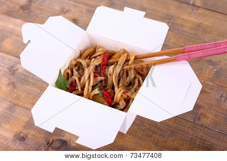 Fried noodles and sticks in takeaway box on wooden background
