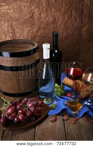 Supper consisting of Camembert and Brie cheese, honey, wine and grapes on napkin in basket and wine barrel on wooden table on brown background