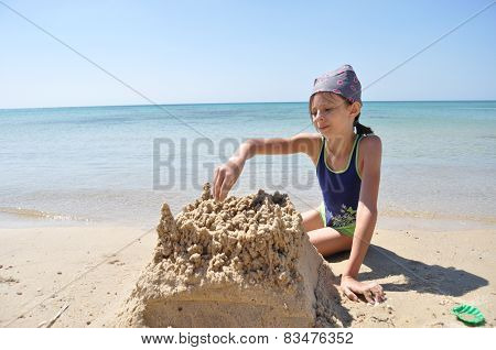 The Girl Builds A Sand Castle On The Beach. Vacation In An Exotic Country