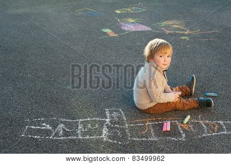 Cute toddler boy drawing with chalk on a nice day outdoors
