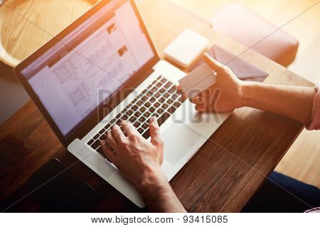 Rear view of male hands holding credit card typing numbers on computer keyboard