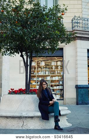 Elegant young university student use digital tablet outdoors while sitting near the tree