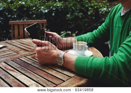 Side view freelancer sitting on the terrace with cup of coffee and touch screen tablet