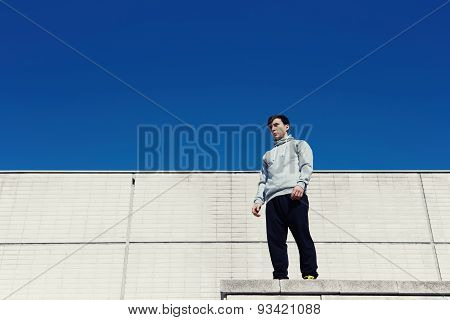 Portreit young parkour standing on the roof on a background of white walls and sky preparing to jump