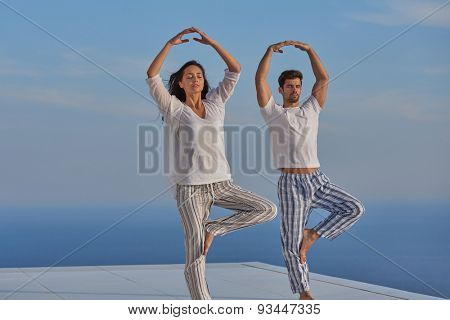 young couple practicing yoga at sunset in modern home terace with ocean and sunset in background