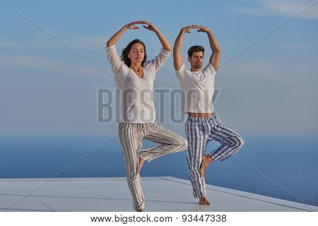 young couple practicing yoga at sunset in modern home terace with ocean and sunset in background