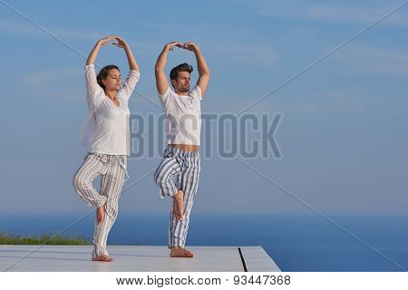 young couple practicing yoga at sunset in modern home terace with ocean and sunset in background