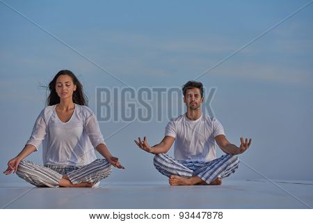 young couple practicing yoga at sunset in modern home terace with ocean and sunset in background
