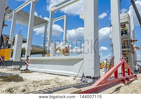 Mobile crane is operating and worker is assembly concrete joist in high place. Height worker is placing truss on building skeleton.
