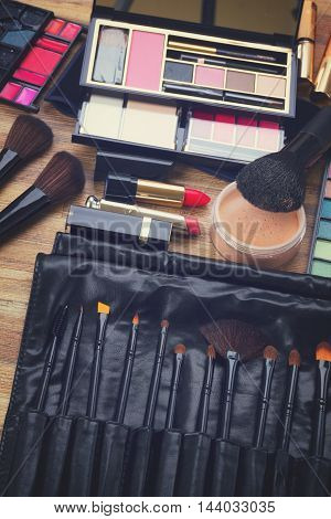 Collection of black make up brushes, lipsticks, maskara, eye shadows and powder, retro toned