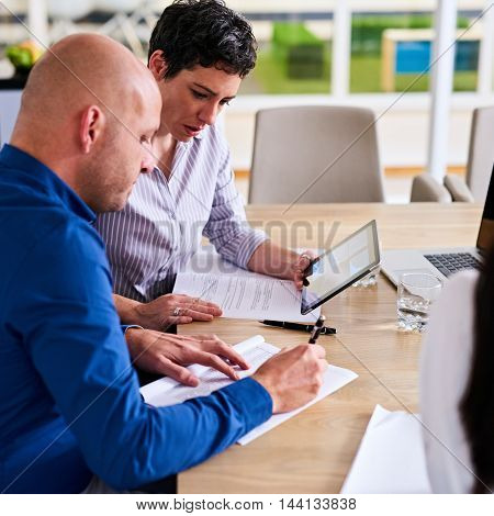 Square image fo caucasian businessman and busineswoman working together in a conference room intergrating technology into their analysis in the form of an electronic tablet.