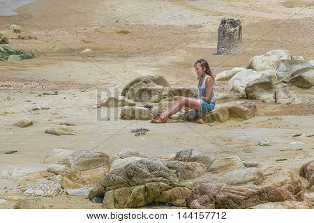 MONTEVIDEO, URUGUAY, - DECEMBER - 2015 - Young woman sitting on rocks at beach in Montevideo Uruguay