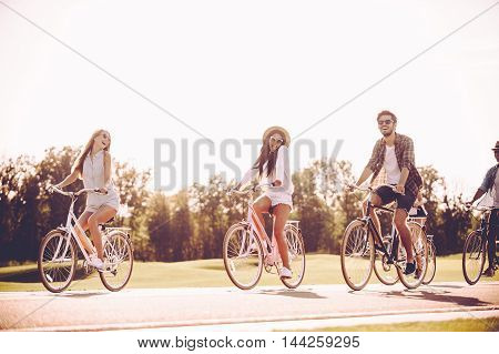 Cycling together is fun. Group of young people riding bicycles along a road and looking happy