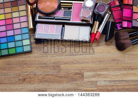 brushes, lipsticks, maskara, eye shadows and powder border on wood, top view with copy space