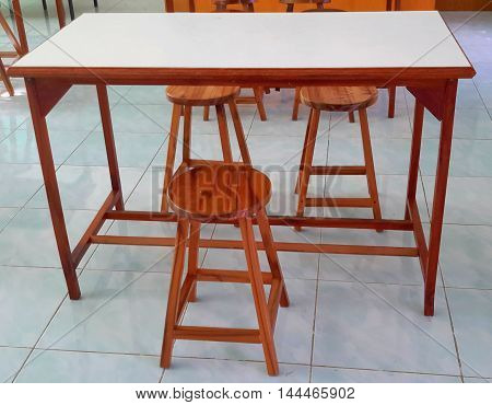 wooden lab table with braced legs, white formica top, and three varnished four-legged wooden stools, on pale blue tile floor, Ranot, Thailand