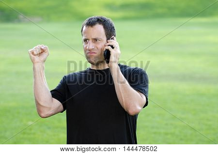 Frustrated angry man on his cell phone outdoors in a black t-shirt.