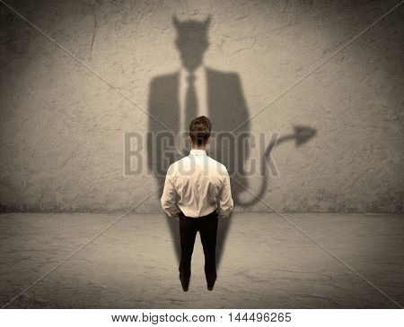 An experienced tricky businessman in suit looking at his devil desguise shadow reflected on the wall concept