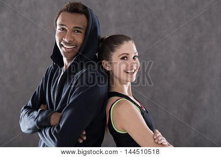 Happy sportspeople in casual clothes standing back to back and smiling to camera. Concept of fitness and health