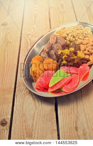 Assorted dry fruits and nuts on plate over wooden background