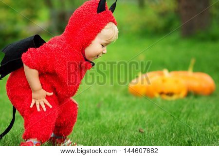 Baby in devil costume with pumpkins. Child in halloween outfit playing in the garden