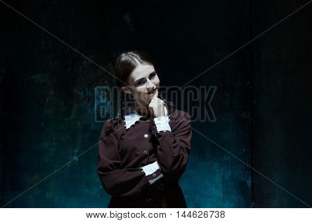 Portrait of a young smiling girl in school uniform as killer woman against school board . The image in the style of Halloween and Addams family
