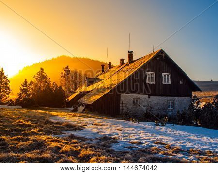 Mountain hut in first beams of rising sun. Freezy mountain morning in winter time.