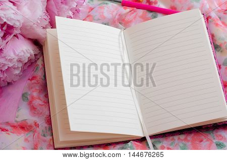 Open pink notebook on a beautiful pink background. Flowers near the notepad