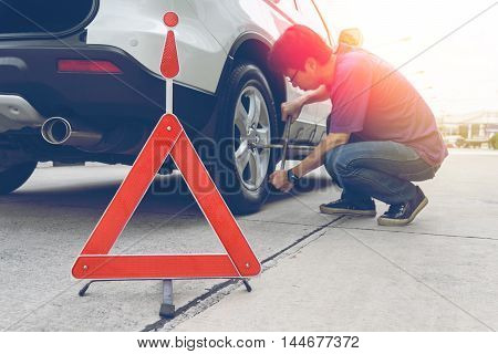 Man loosening lug nuts on his car flat tire. broken down car