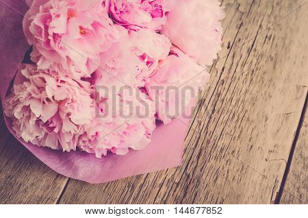 Bouquet of peonies in a pink wrapper on a wooden background (vintage)