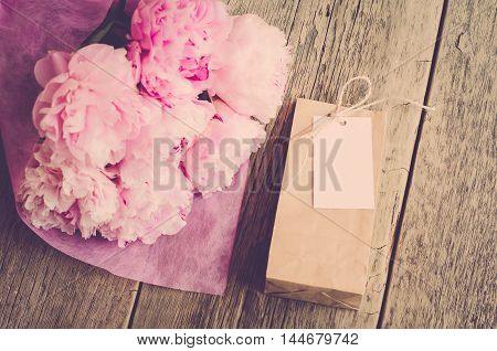 Gift for women: flowers peonies and kraft bag with white tag on wooden background (vintage)