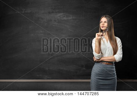 Young businesswoman standing in front of blank blackboard. Business staff. School and education. Office clothes. Learning and teaching.