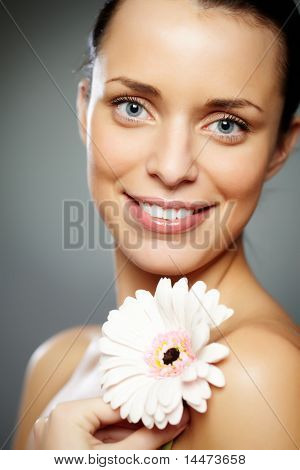 Wunderschöne Frau mit Herbera Blick in die Kamera mit Lächeln auf grauem Hintergrund