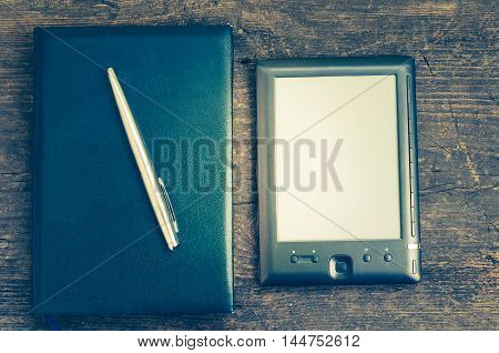 Black ereader with notebook in leather cover and ink pen on vintage old rustic wooden table. Blank E-book reader. New technologies in education. Back to school concept. Top view. Copy space.