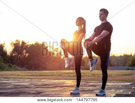 Young caucasian man and woman warming up before exercising or jogging outdoors. Fitness workout.