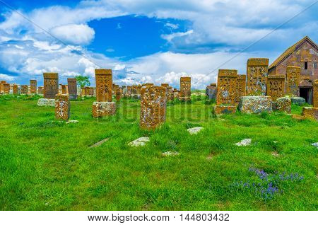 The red khachkars of Noratus Cemetery covered with lichen and moss surrounded by green grass and wildflowers Gegharkunik Province Armenia.
