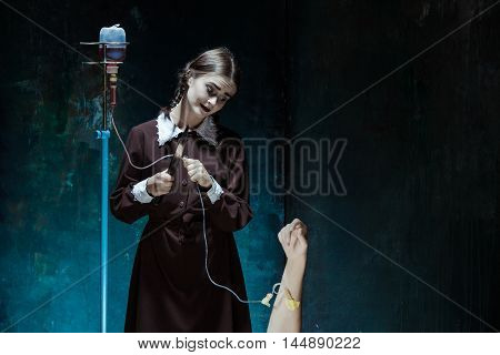 Portrait of a young girl with knife and drop counter in school uniform as killer woman against school board . The image in the style of Halloween and Addams family