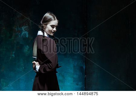 Portrait of a young girl with knife in school uniform as killer woman against school board . The image in the style of Halloween and Addams family