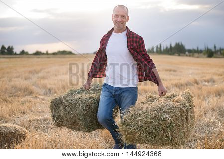 Portrait Of Farmer And Harvest. Strawbale In Hands