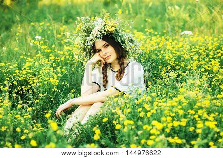 Beautiful Girl In Wreath Of Flowers  In Meadow On Sunny Day. Portrait Of Young Beautiful Woman Weari