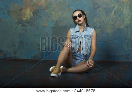 Style Vogue And Denim Sexy Young Slender Girl With Red Lips Wearing Glasses Dressed In A Denim Suit 