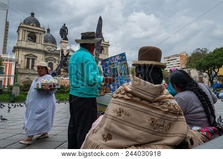 LA PAZ, BOLIVIA - 24 MARCH, 2018: Two indigenous bolivian women sit on the stairs at Plaza Murillo and buy icecream from street vendor