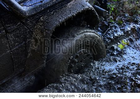 Fragfment Of Car Stuck In Dirt, Close Up. Dirty Offroad Tire Covered With Mud. Wheel With Cloud Of S
