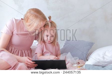 Young Attractive Blond Woman With Her Little Charming Daughter In Pink Dresses Seriosly Watching Som