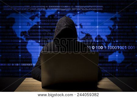 Hacker In A Jacket With A Hood With A Laptop Sits At The Table. Added Identity Theft Icons, Account 