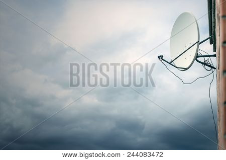 Sattelite Dish Tv Antenna On The Brickwall On A Thunderclouds Background.