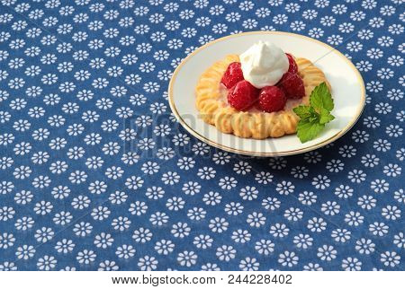 One Rasperry Tart On A Blue Tablecloth With White Flowers