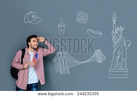 Visiting The Usa. Cheerful Active Tourist Holding A Little Flag Of The Usa And Feeling Impressed Whi