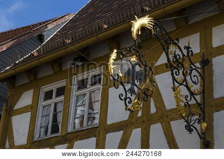 Two Windows On Old Multicolored Wooden Country House. Forged Openwork Coat Of Arms On The House In T