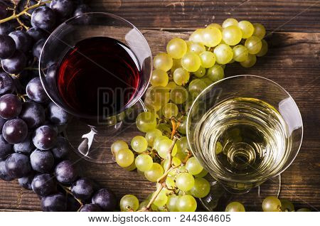 On Rustic Wooden Table Glasses Of White And Red Wine, With Mixed Grapes