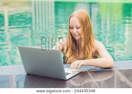 Young Female Freelancer Sitting Near The Pool With Her Laptop In The Hotel Browsing In Her Smartphon